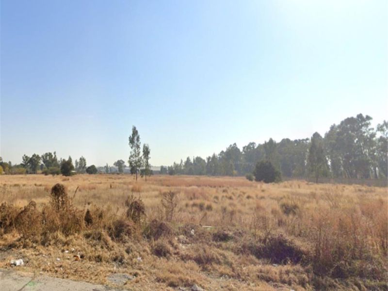 A wide-angle view of an undeveloped industrial land plot featuring dry vegetation and open space.
