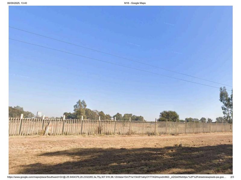 A view of an industrial property perimeter featuring concrete palisade fencing and an unpaved ground area.