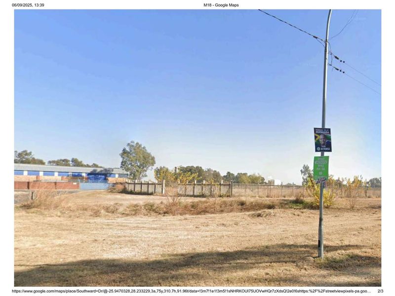 A view of an undeveloped industrial plot featuring perimeter fencing and a utility pole, showing significant overgrown vegetation and unimproved ground.
