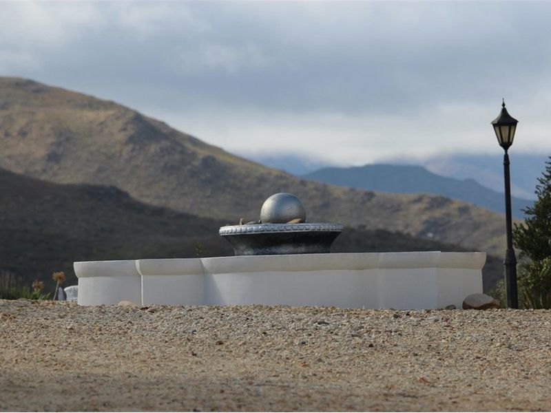 A landscaped garden area featuring a decorative water fountain and a classic lamp post, set against a scenic mountain backdrop.