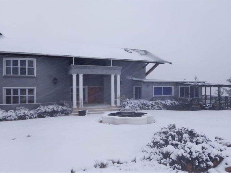 Front elevation of a large farmhouse featuring a covered entrance with classical columns, a central stone fountain, and a side timber pergola.