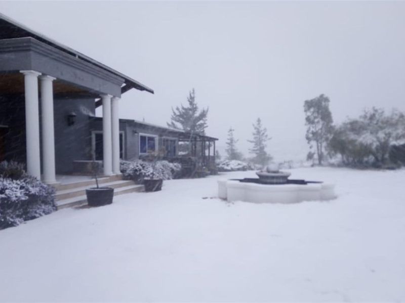 A rear view of the farmhouse featuring a covered patio with columns and a stone fountain, captured during a winter snowfall.