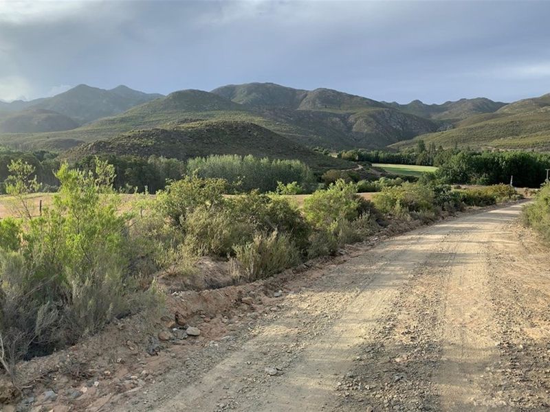 A scenic view of the rural farm landscape featuring a gravel access road, rolling hills, and mountain vistas.