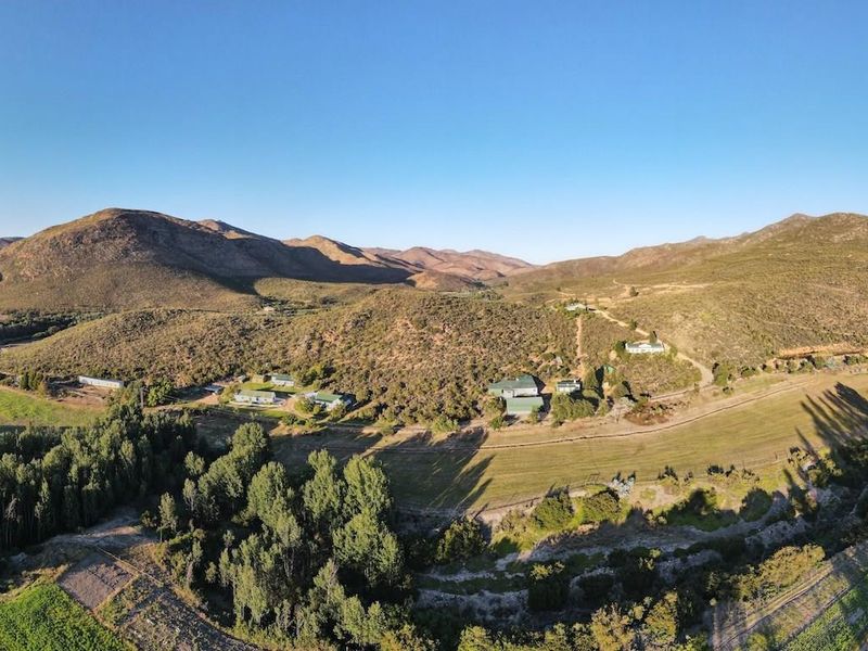 An expansive aerial view of a rural farm property set against a scenic mountain landscape with surrounding fields and natural vegetation.