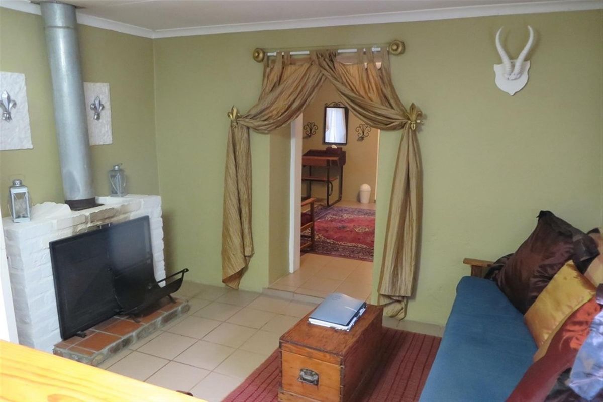 A living room featuring a brick fireplace with a metal flue and tiled flooring, providing a cozy atmosphere with access to an adjacent room.
