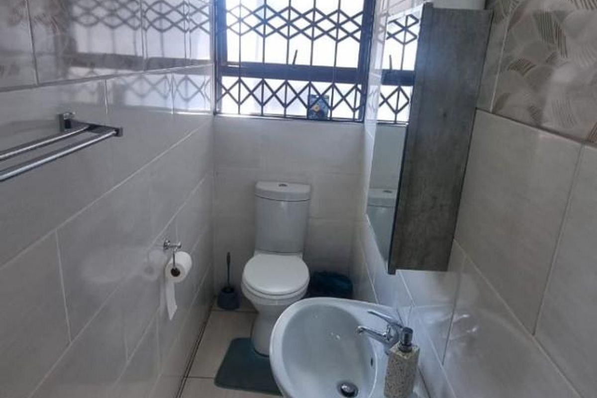 A compact guest bathroom featuring floor-to-ceiling wall tiles, a pedestal basin, a toilet, and a window with security bars.