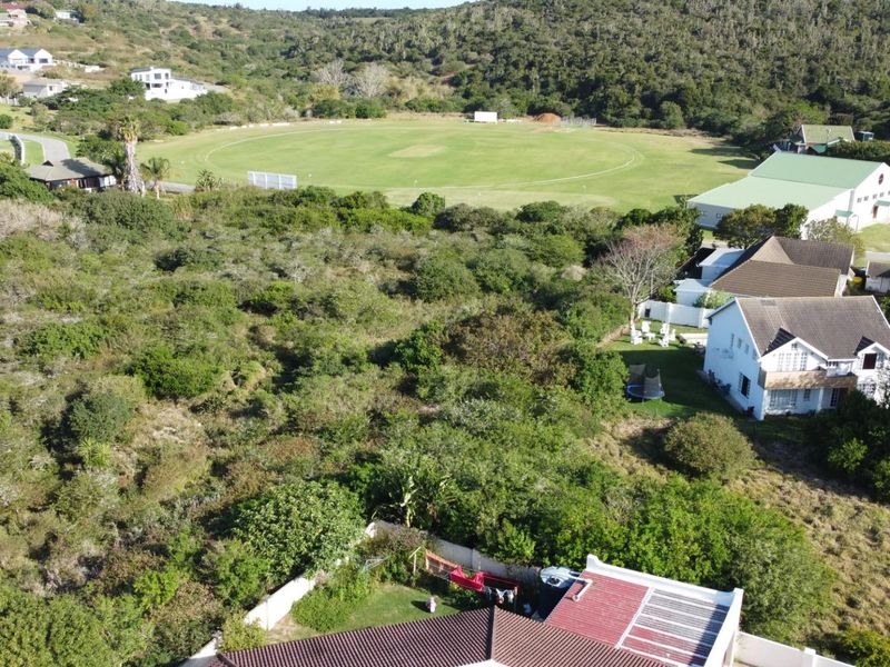 Aerial view of a vacant residential plot featuring dense natural vegetation, situated in a scenic neighborhood near a sports field.