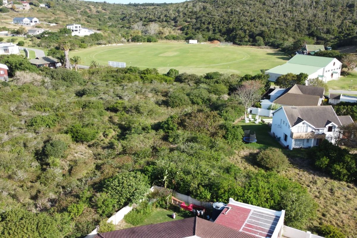 Aerial view of a vacant residential plot featuring dense natural vegetation, situated in a scenic neighborhood near a sports field.