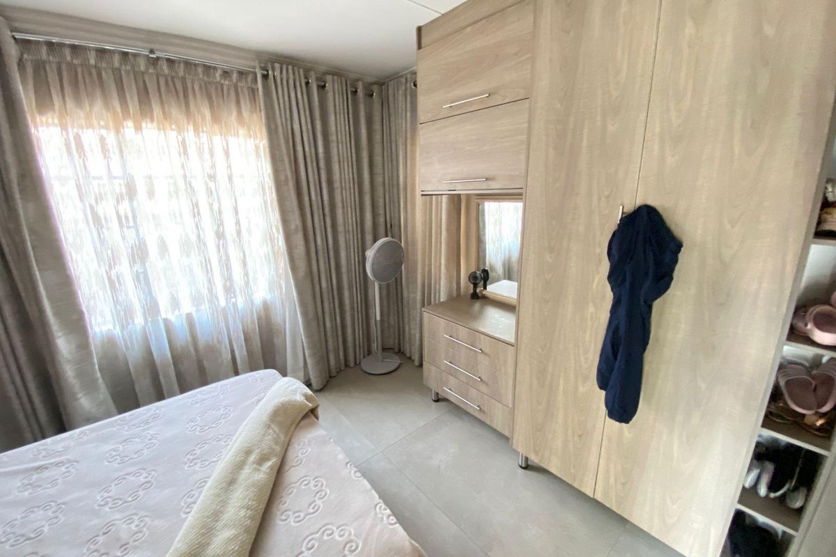 A well-maintained bedroom featuring light wood-toned built-in cabinetry, tiled flooring, and floor-to-ceiling curtains.