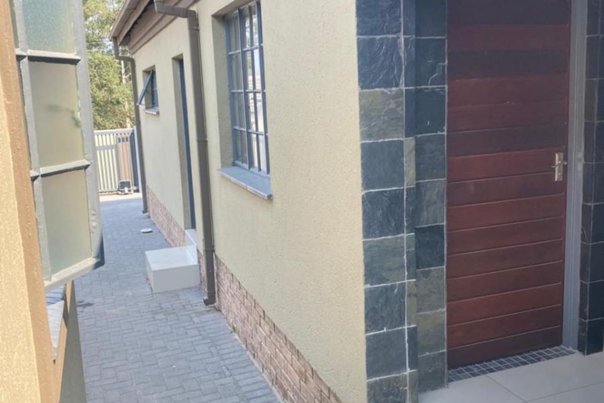 A side exterior view of the property featuring a paved walkway, a wooden entrance door with stone tile surround, and tiled steps.