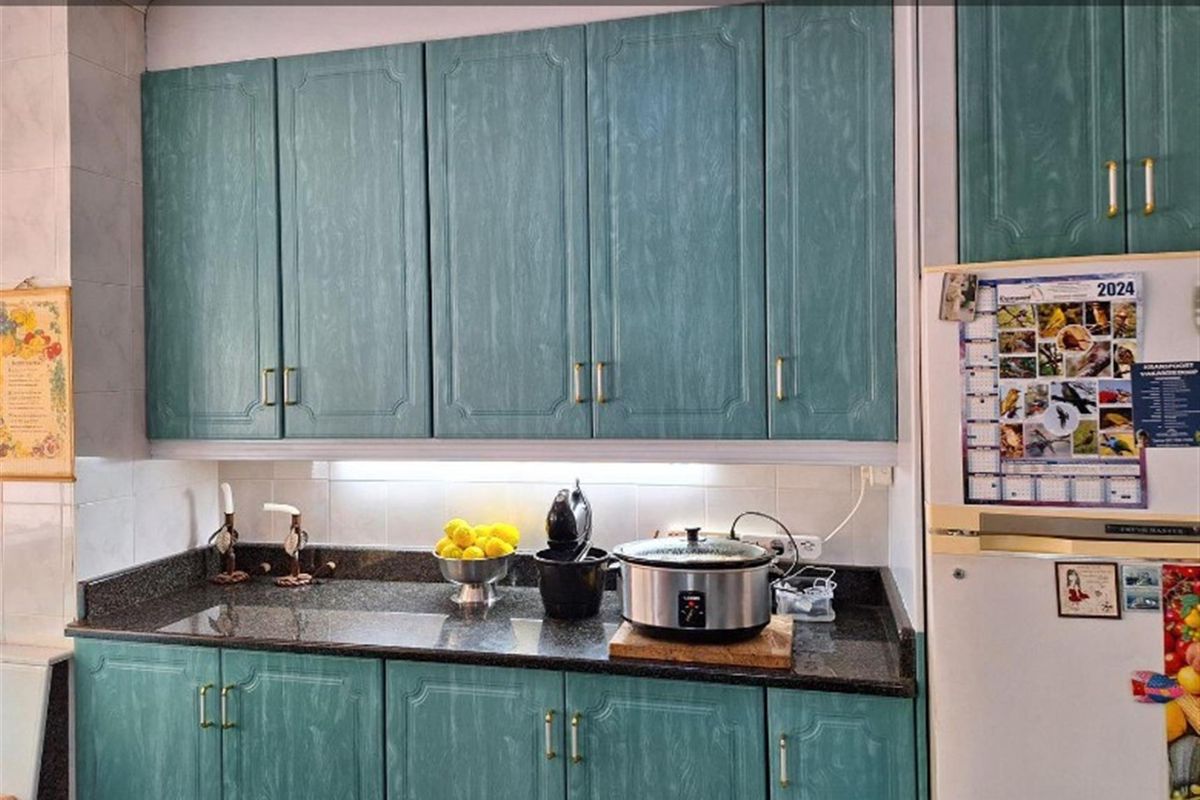 A kitchen area featuring teal-toned cabinetry, dark granite countertops, and tiled backsplash, providing a functional workspace.