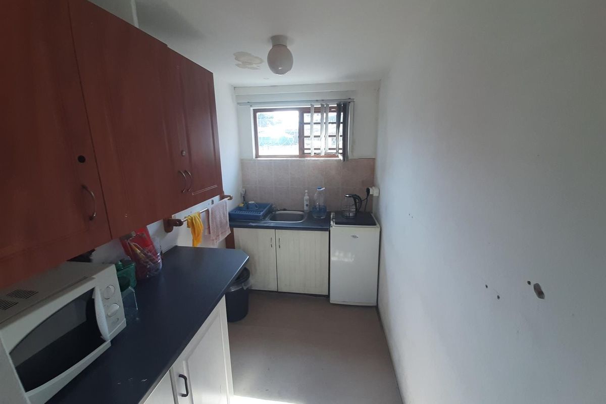 A compact kitchenette featuring built-in cabinetry, a single basin sink, and laminate countertops, requiring cosmetic updates to improve its overall condition.