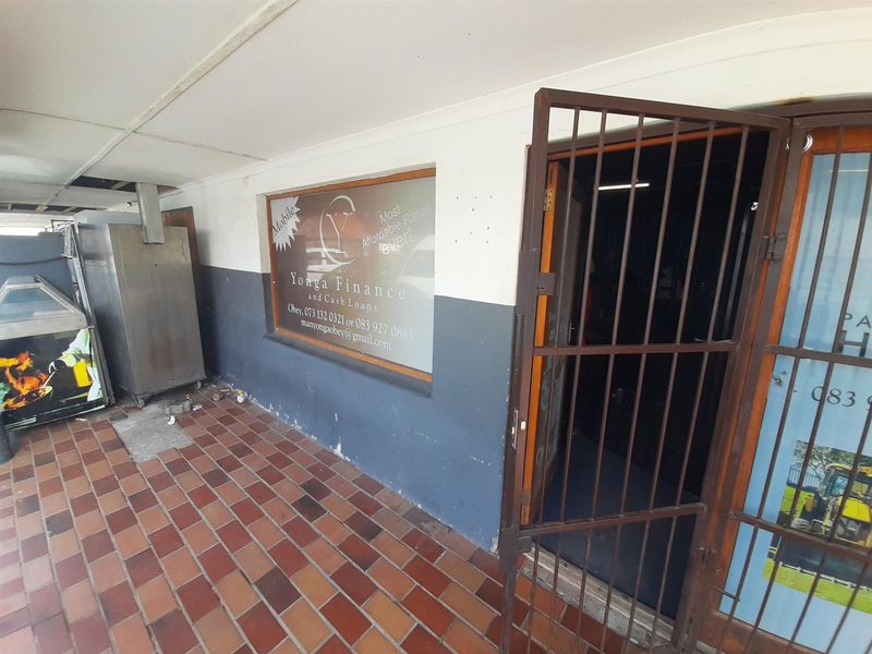 Commercial storefront entrance featuring a tiled walkway, metal security gate, and large display window with business signage.