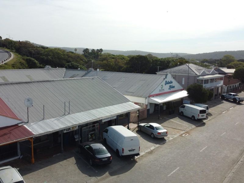 Aerial view of a commercial strip center featuring multiple storefronts with corrugated metal roofing and paved parking area.