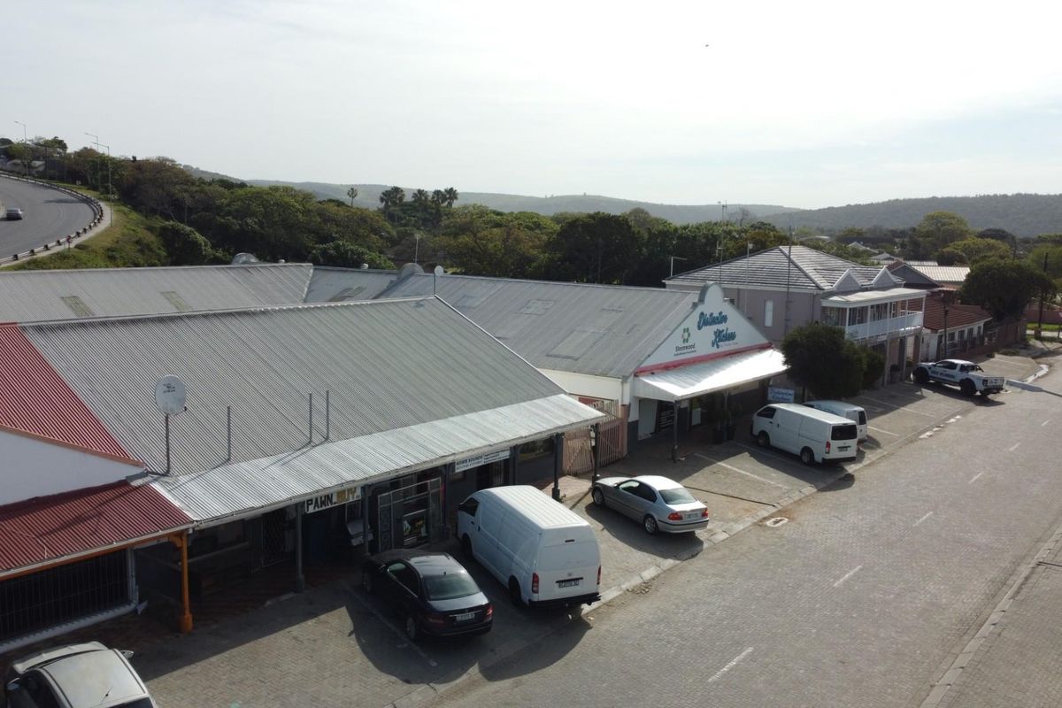 Aerial view of a commercial strip center featuring multiple storefronts with corrugated metal roofing and paved parking area.