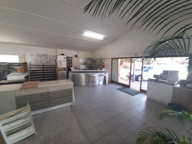 Spacious commercial showroom or retail area featuring tiled flooring, a built-in service counter, and large sliding glass doors providing natural light and street access.