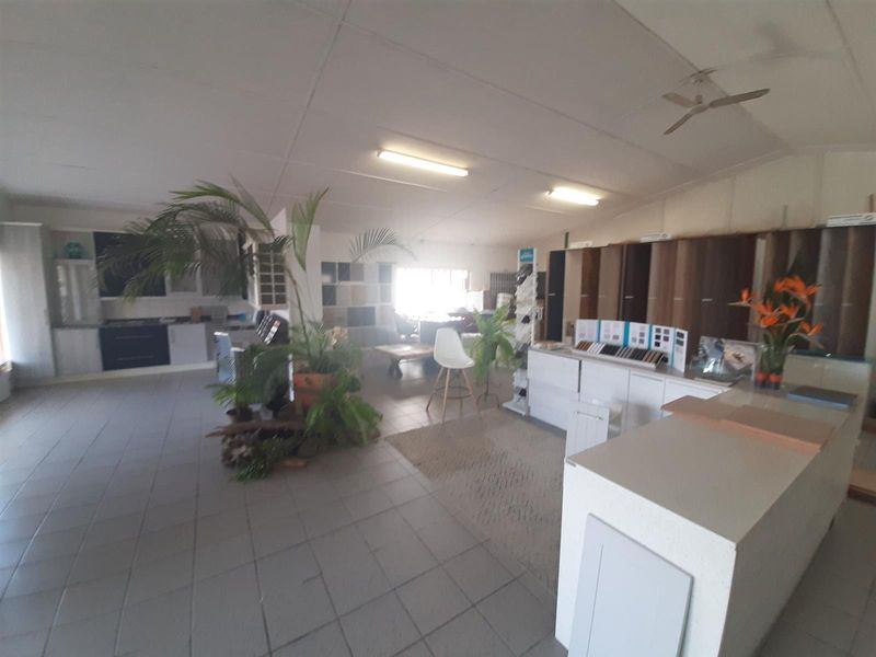 Spacious commercial showroom featuring tiled flooring, integrated cabinetry, and overhead fluorescent lighting, suitable for retail or office display purposes.