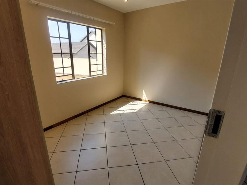 A bright, empty bedroom featuring neutral wall tones, tiled flooring, and a grid-pattern window providing natural light.