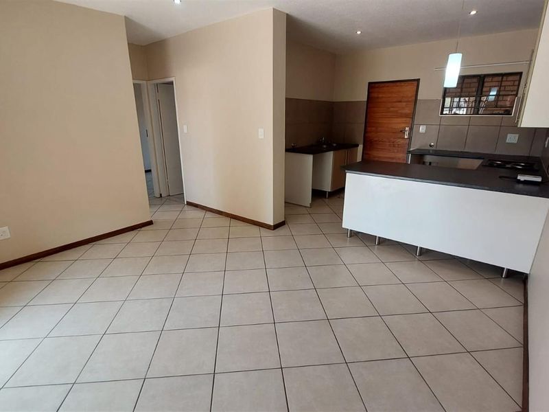 An open-plan living and kitchen area featuring neutral tiled flooring, modern cabinetry, and a functional kitchen island with a built-in hob.