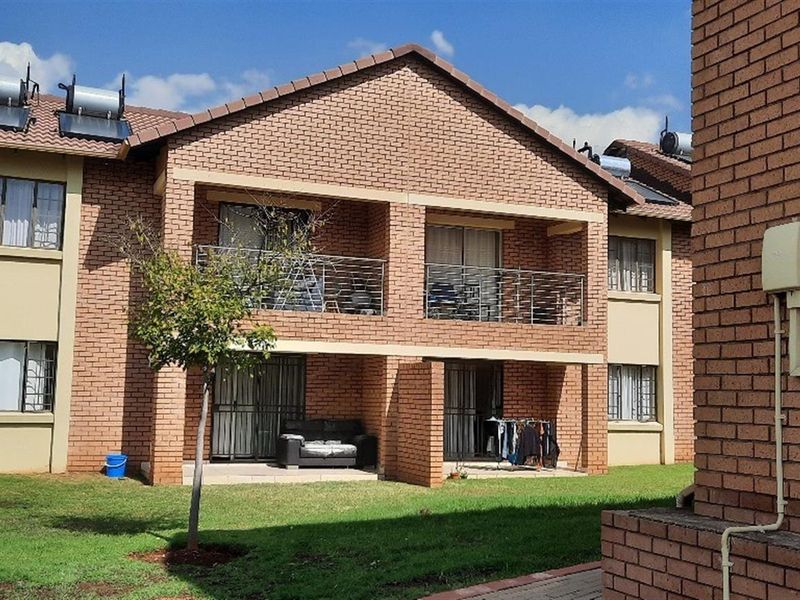 Rear view of a face brick townhouse complex featuring ground floor patios, upper-level balconies with metal railings, and roof-mounted solar water heating systems.