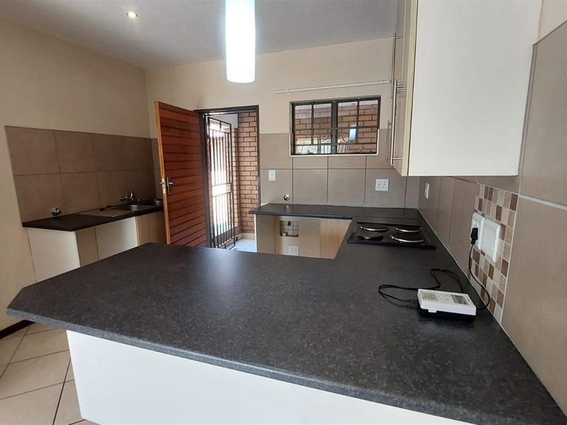 A functional kitchen featuring laminate countertops, built-in cabinetry, an electric hob, and tiled splashbacks, offering a clean and practical workspace.