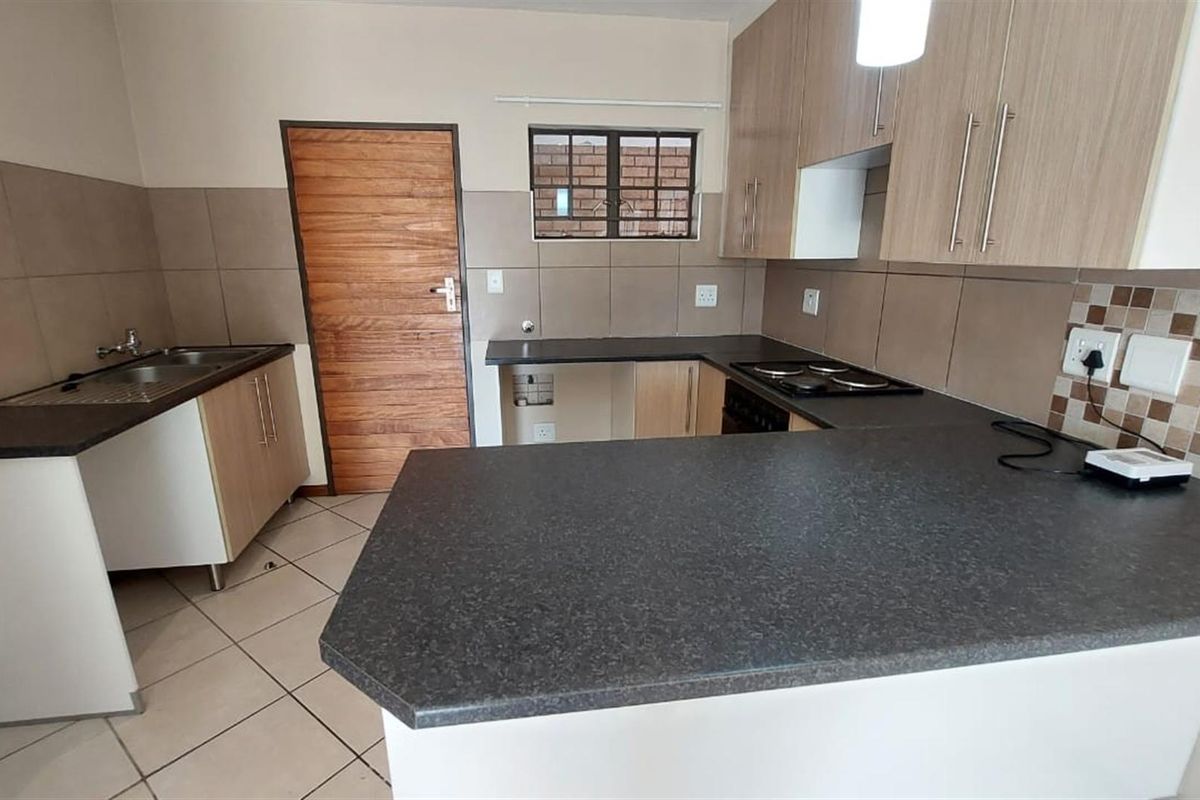 A clean, functional kitchen featuring laminate cabinetry, dark countertops, a built-in electric hob, and neutral tiled flooring.