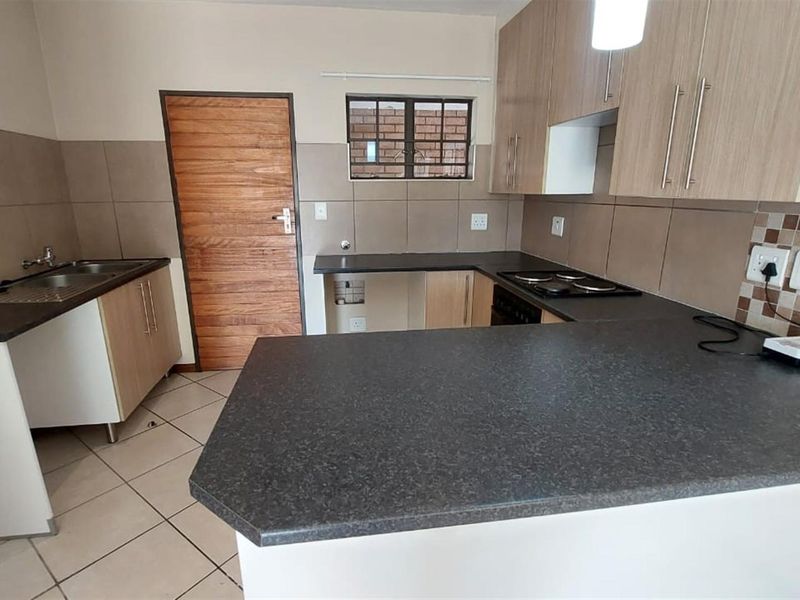 A clean, functional kitchen featuring laminate cabinetry, dark countertops, a built-in electric hob, and neutral tiled flooring.