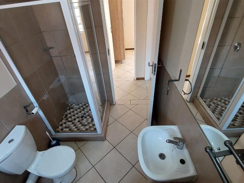 A functional bathroom featuring a shower enclosure, pedestal basin, and toilet with neutral wall and floor tiling.