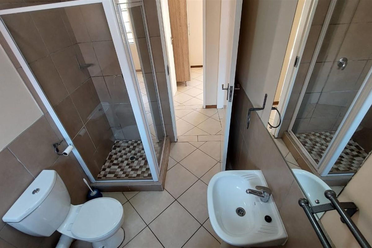 A functional bathroom featuring a shower enclosure, pedestal basin, and toilet with neutral wall and floor tiling.