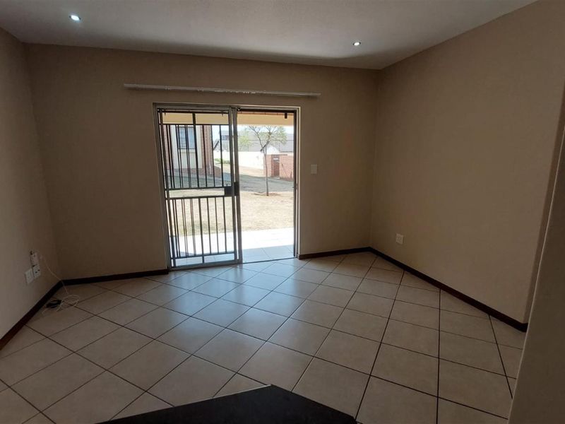 An empty, neutrally painted living room featuring tiled flooring, recessed lighting, and a sliding glass door with a security gate leading to the exterior.