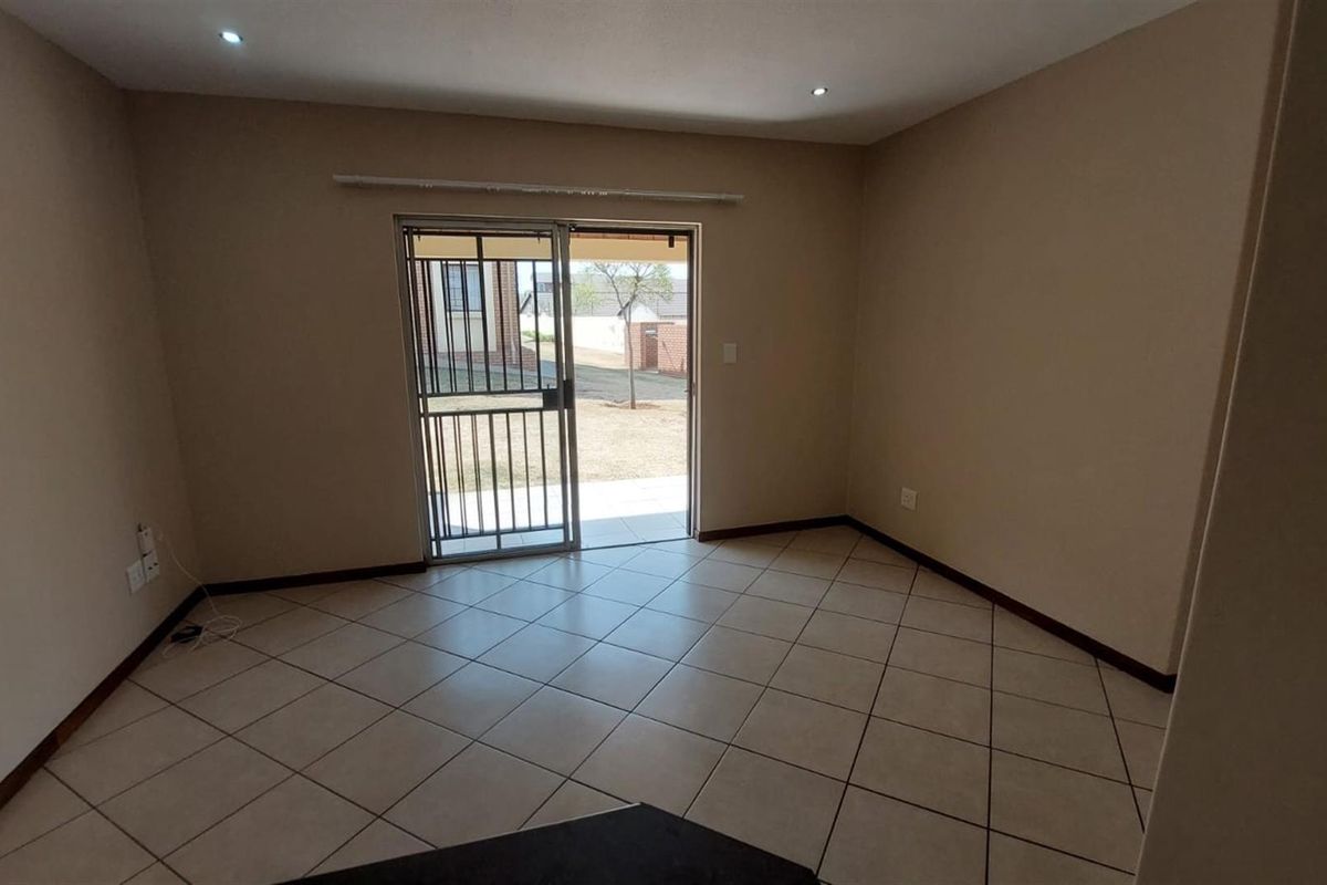 An empty, neutrally painted living room featuring tiled flooring, recessed lighting, and a sliding glass door with a security gate leading to the exterior.
