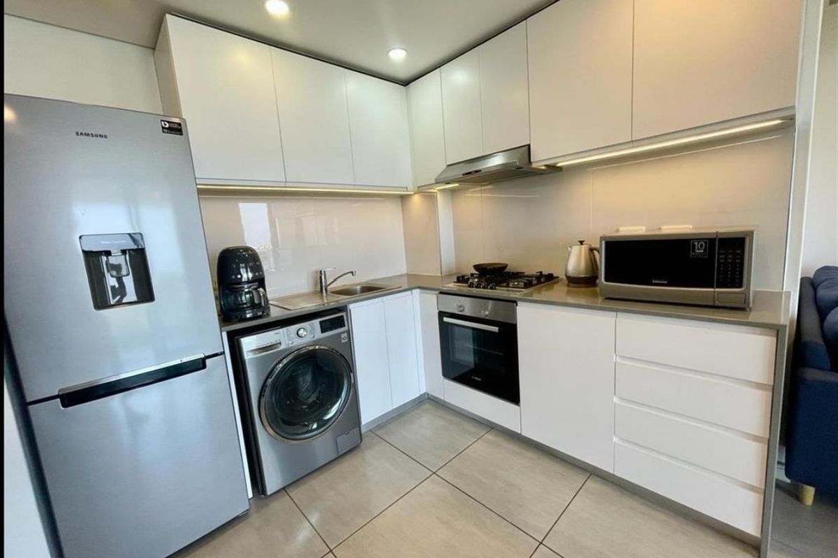 Modern kitchen featuring sleek white cabinetry, stone countertops, integrated gas hob, oven, extractor fan, and tiled flooring in a clean, contemporary layout.