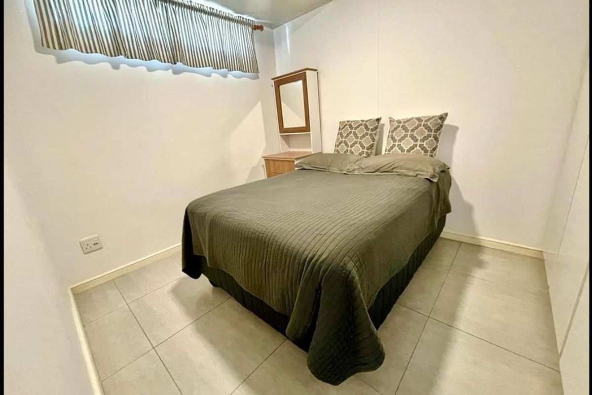 A compact bedroom featuring neutral tiled flooring and a built-in cupboard, providing a functional and clean living space.