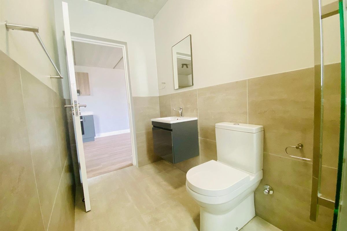 A modern bathroom featuring a wall-mounted vanity, a sleek toilet, and neutral wall tiling, with a view into the adjacent living area.