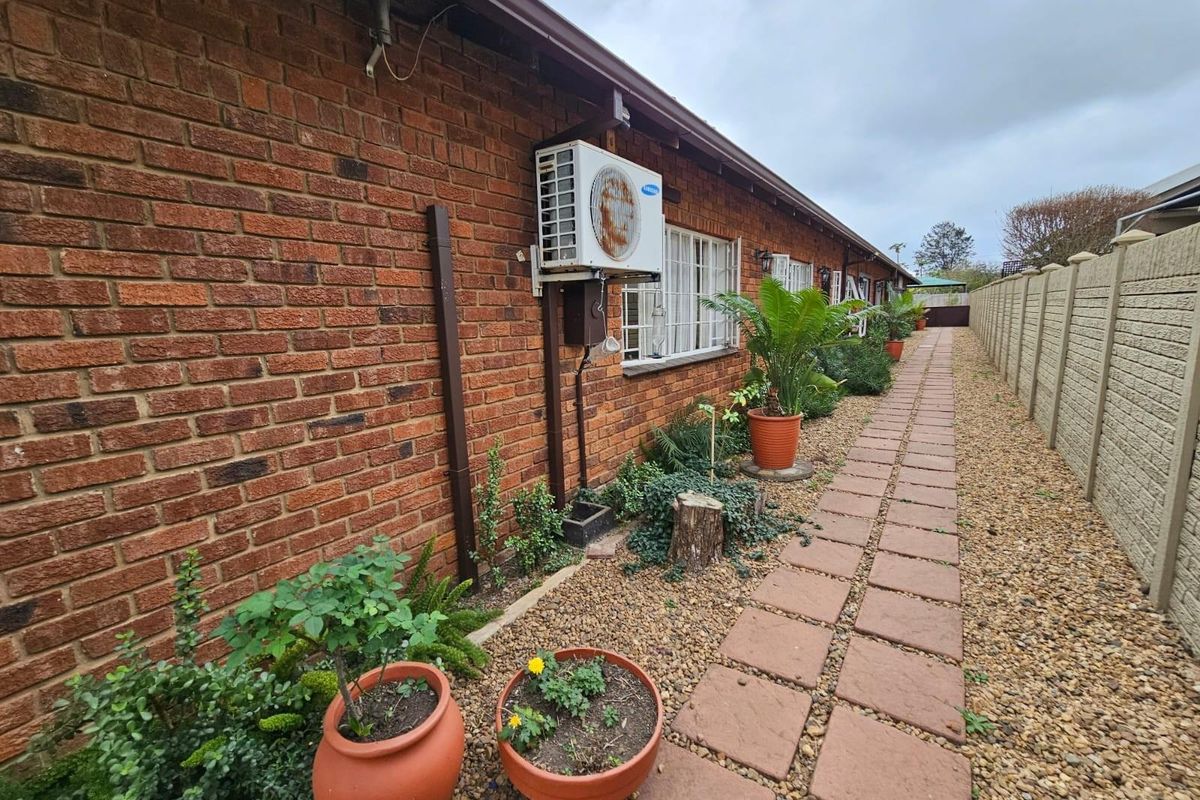 A side exterior view of the house featuring a brick facade, paved walkway, gravel landscaping, and a wall-mounted air conditioning unit.