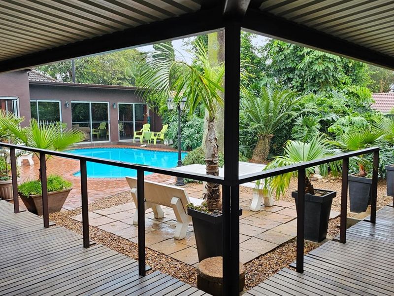 A covered patio overlooking a private swimming pool and landscaped garden area, featuring timber decking and metal structural supports.