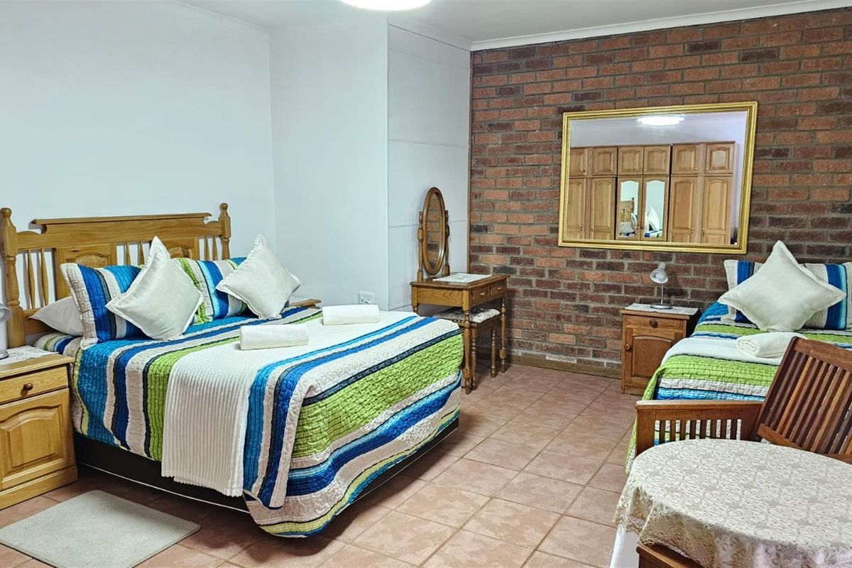 Spacious bedroom featuring a rustic exposed brick feature wall, tiled flooring, and built-in wooden cabinetry.