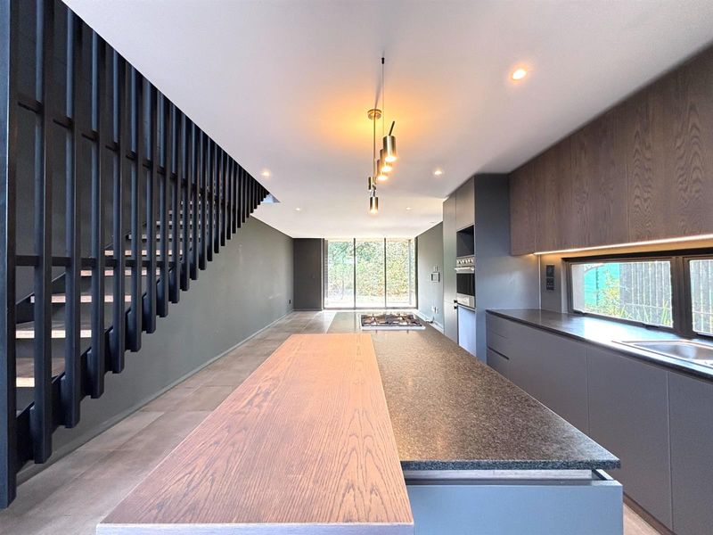 Modern open-plan kitchen featuring a large island, sleek cabinetry, built-in appliances, and a striking staircase, leading to a bright living area.