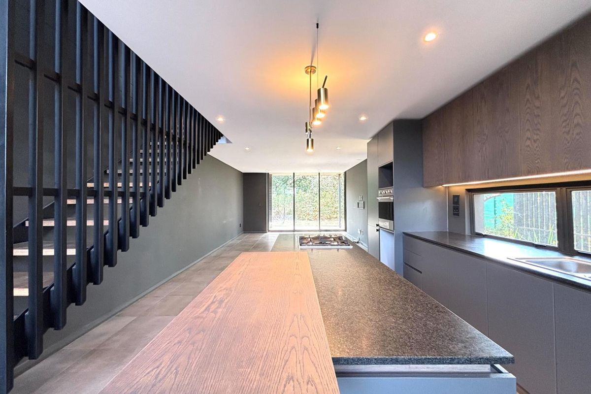 Modern open-plan kitchen featuring a large island, sleek cabinetry, built-in appliances, and a striking staircase, leading to a bright living area.