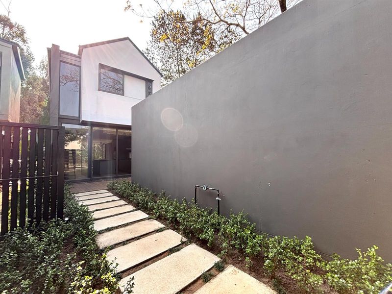 A modern townhouse rear exterior featuring a stone paver walkway, landscaped garden beds, and a large boundary wall leading to the main dwelling.