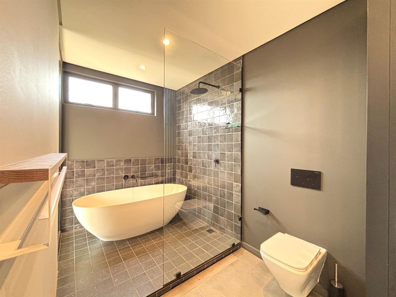 Modern bathroom featuring a sleek freestanding bathtub, a spacious walk-in shower with glass enclosure, and a wall-mounted toilet with contemporary dark tile finishes.