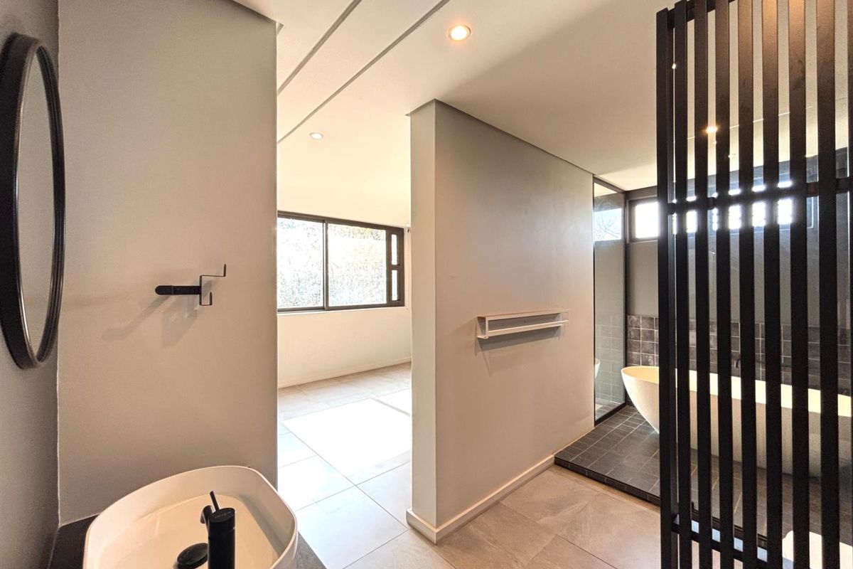 Modern bathroom featuring a freestanding bathtub, vessel sink with black fixtures, and a stylish slatted room divider, finished with contemporary floor tiles.