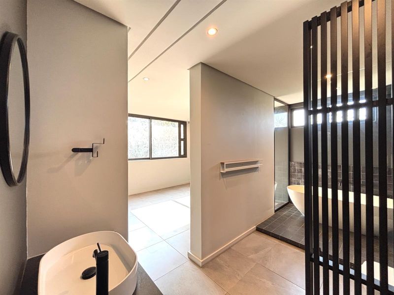 Modern bathroom featuring a freestanding bathtub, vessel sink with black fixtures, and a stylish slatted room divider, finished with contemporary floor tiles.