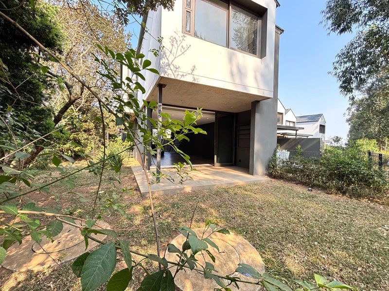 Rear view of a modern townhouse featuring a concrete patio, large sliding glass doors, and a private garden area.