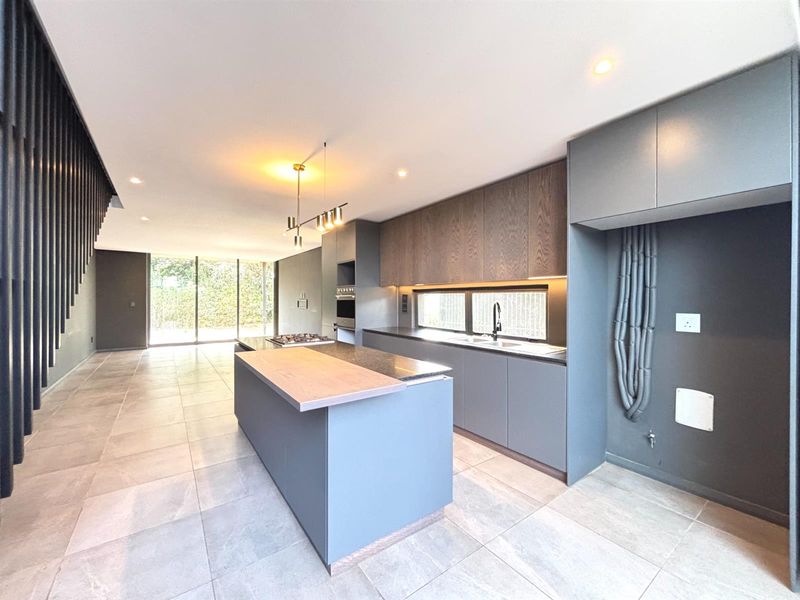 Modern open-plan kitchen featuring a central island, sleek cabinetry, built-in appliances, and tiled flooring, seamlessly flowing into the living area with large glass doors.
