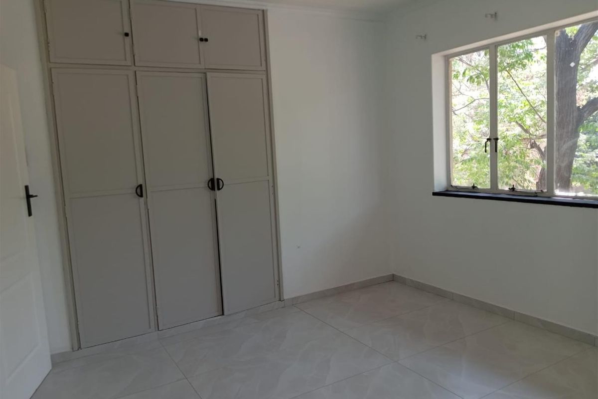 A bright, empty bedroom featuring built-in cupboards and tiled flooring, offering a clean and neutral space ready for personalization.