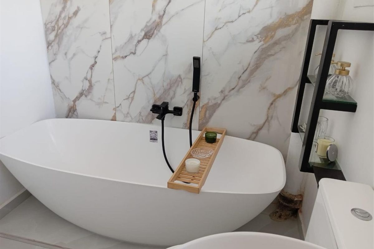 Modern bathroom featuring a freestanding bathtub with matte black fixtures and elegant marble-look wall tiling.