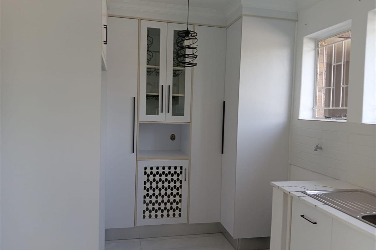 Modern kitchen area featuring white cabinetry, built-in storage, a stainless steel sink, and a decorative patterned cabinet door.