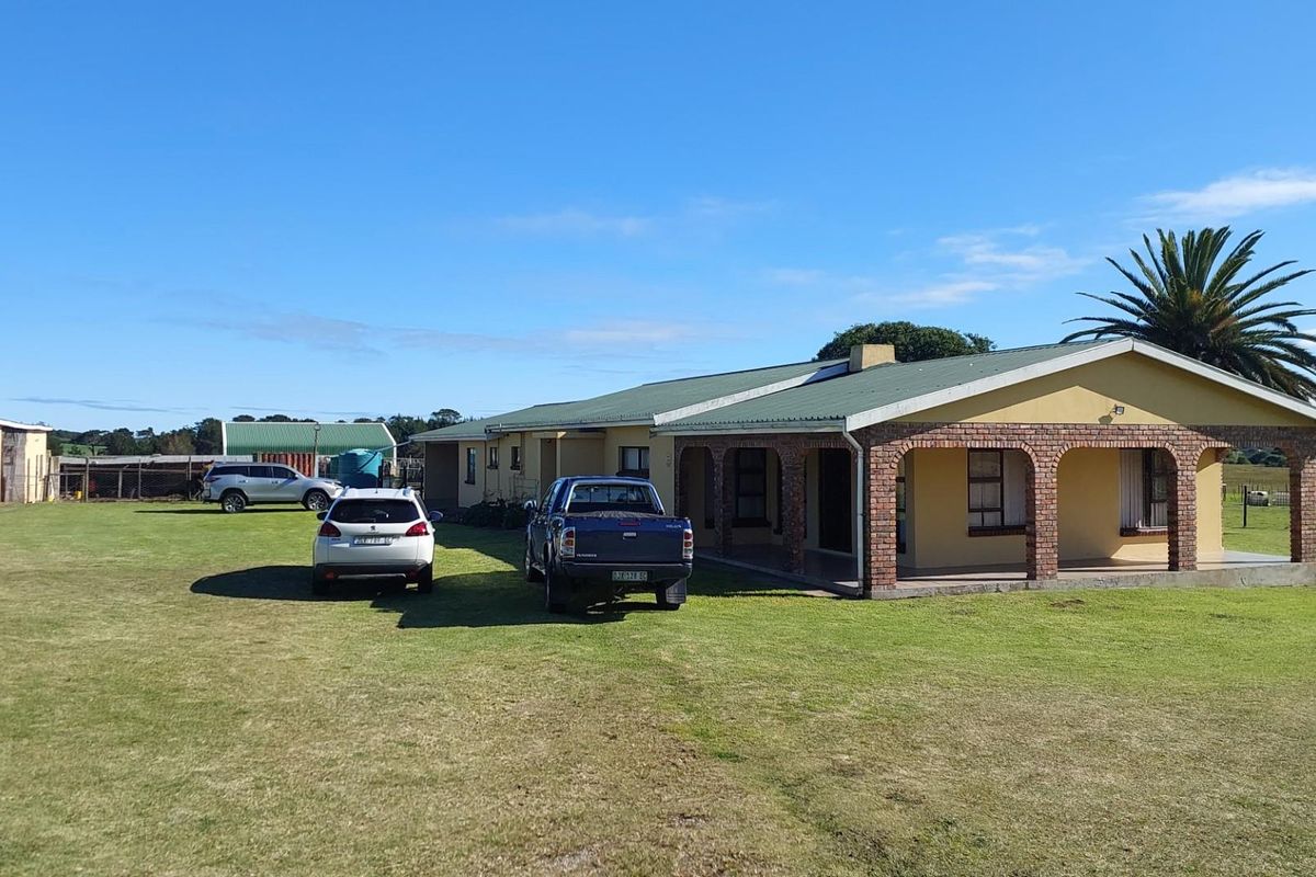 Rear view of a farm property featuring a covered patio with brick archways, a corrugated metal roof, and surrounding outbuildings on a large lawn.
