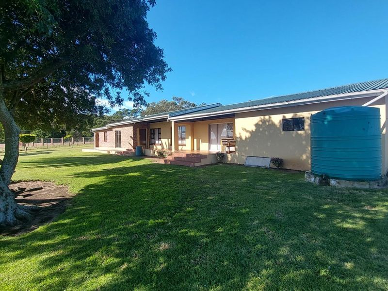 Rear view of the farm property featuring a spacious lawn, covered patio area, and an external water storage tank.